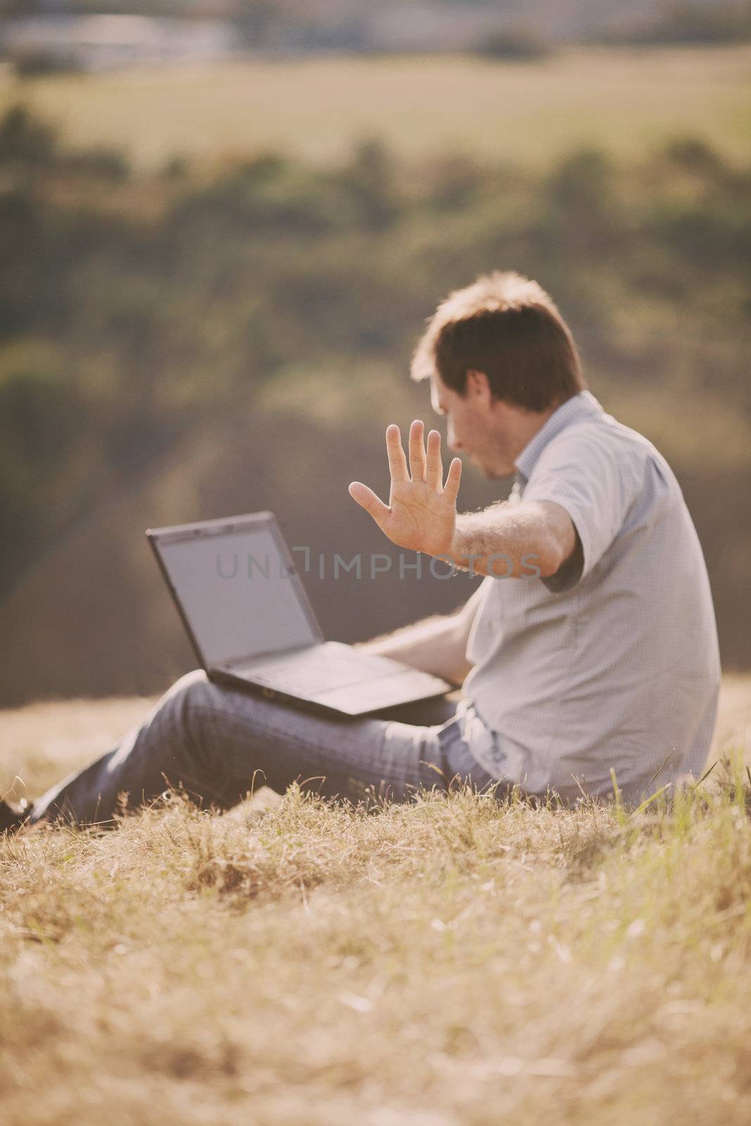 young man using laptop sitting on the grass on the hillside by jannyjus