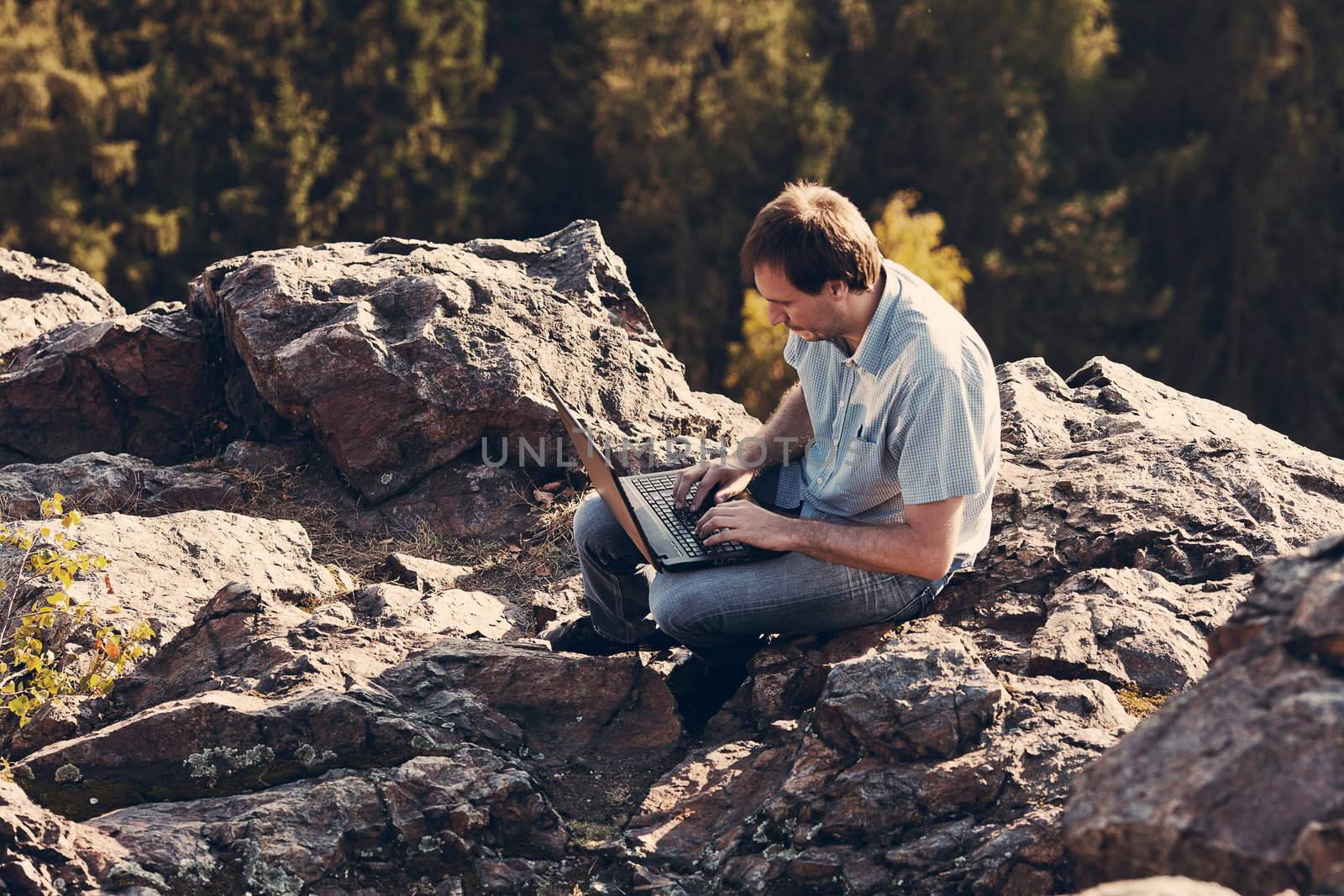 young man using laptop sitting on a rock slope