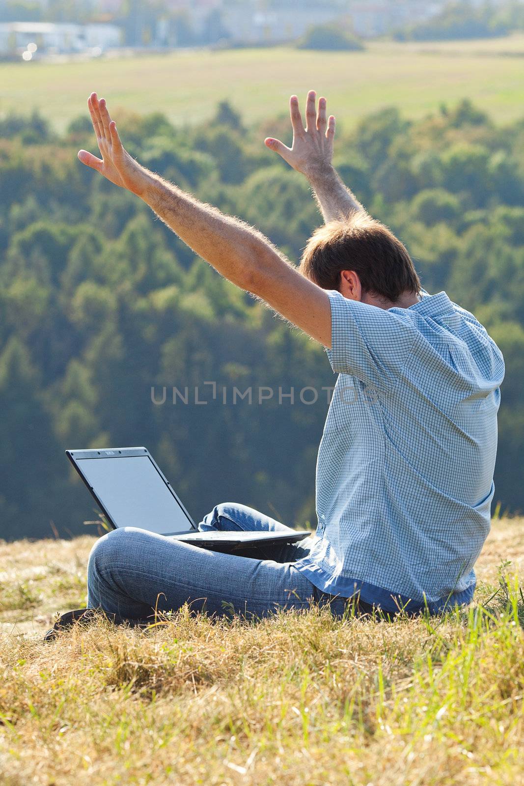 young man using laptop sitting on the grass on the hillside