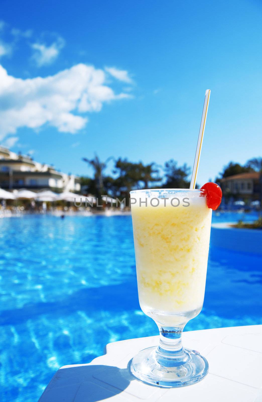 cocktail in glass with a cherry on a background blue water of pool