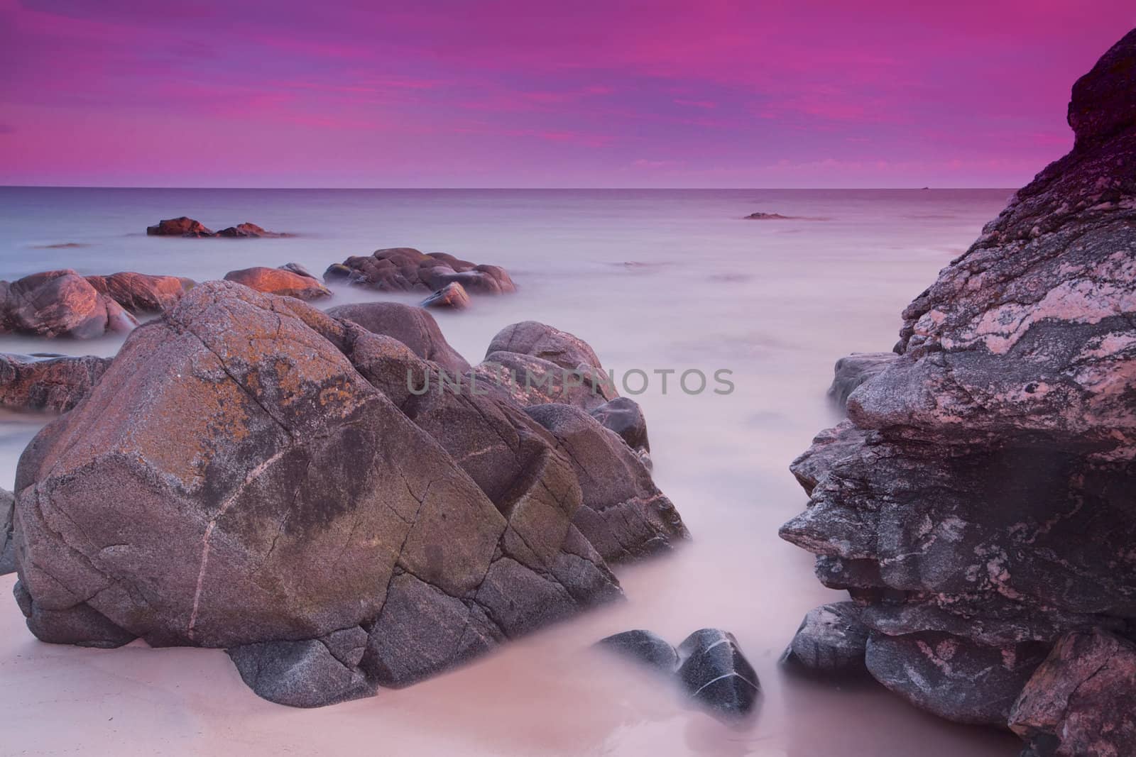 Long exposure of purple evening skies over ocean with large rocks near the shore
