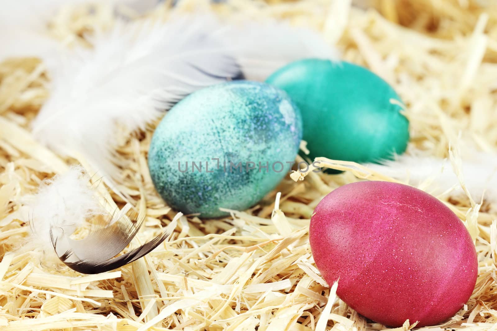 Three colored Easter eggs hidden in straw.