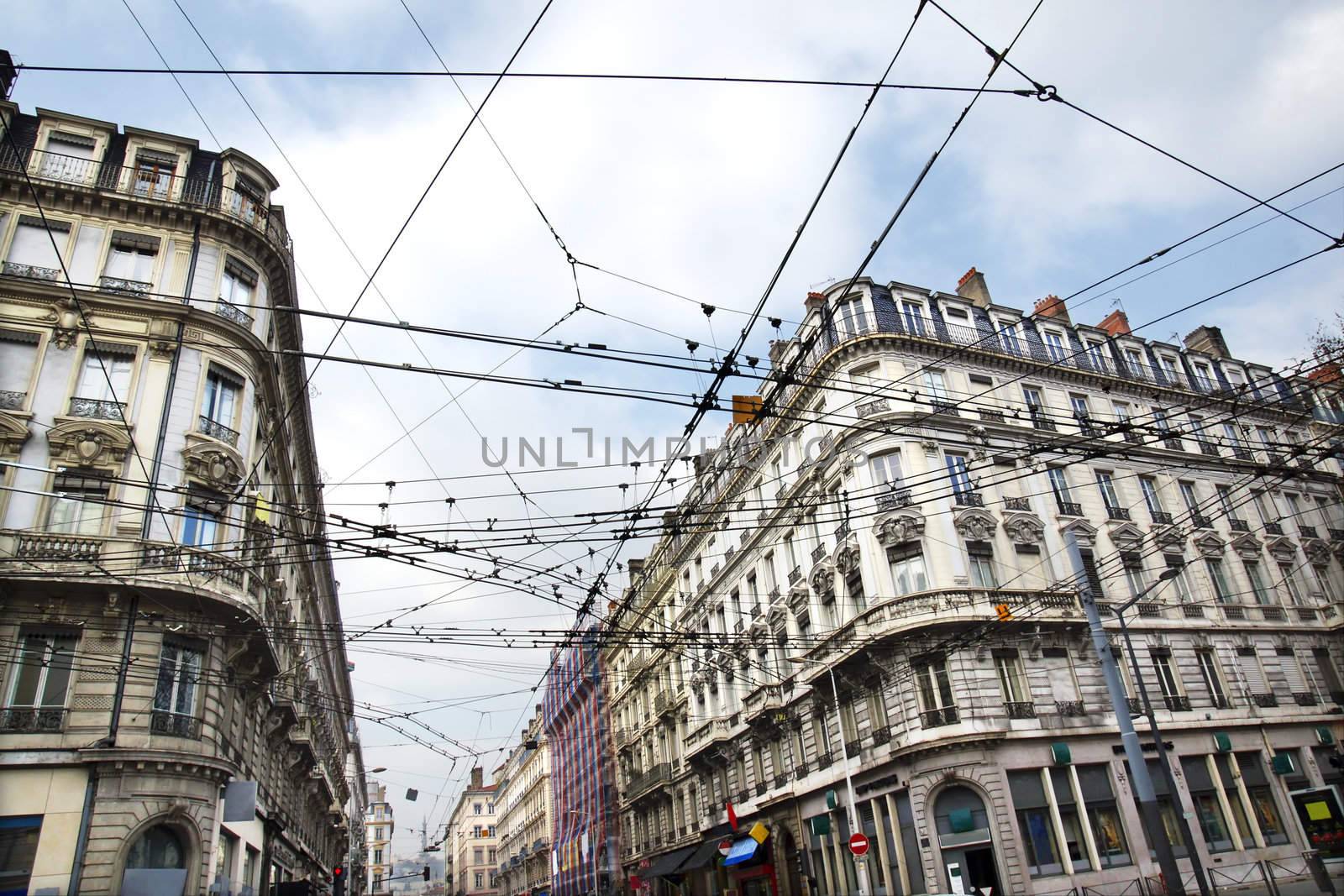 Modern public transportation with tramway or trolley cables criss-crossing at a busy street intersection contrasting with the old historic building architecture of European city, Lyon, France.