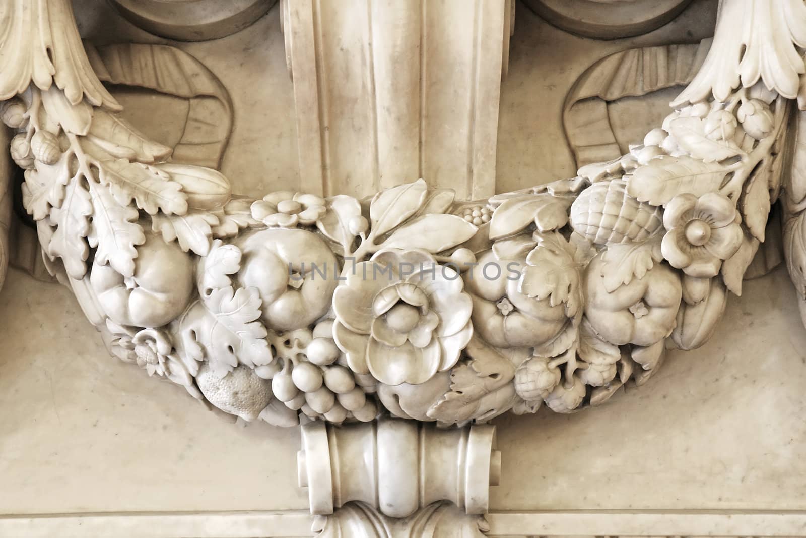 Beautiful detailed carving of a garland with leaves, flowers and fruits part of the marble stone mantle of a luxurious fireplace.