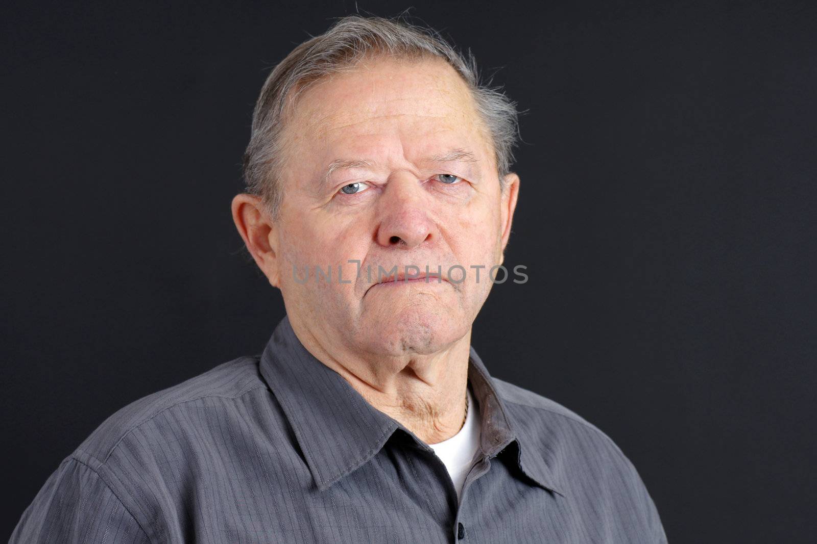 Portrait of a senior man looking very serious, sad or depressed looking at camera with blue eyes, great details, shot in studio over black.