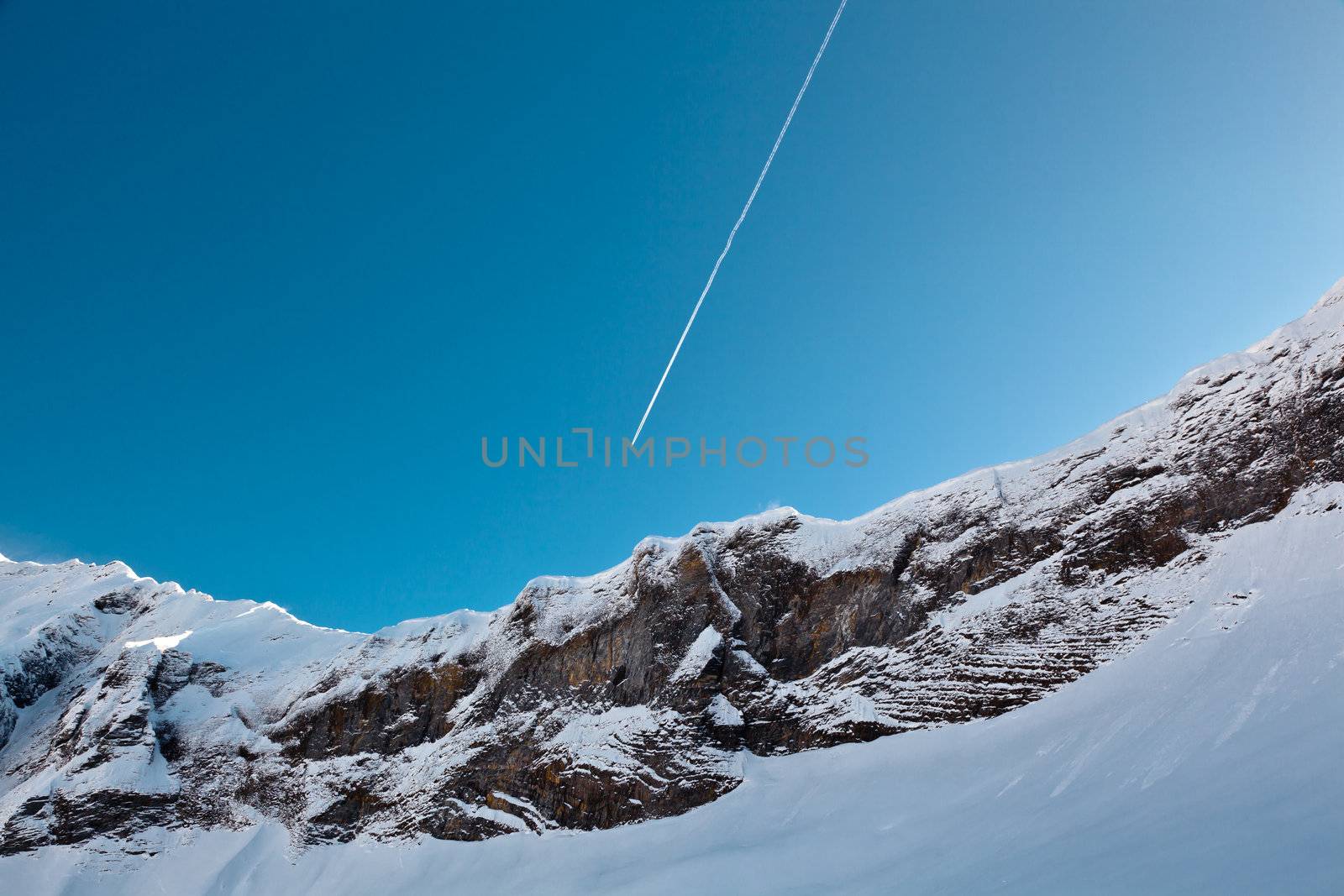 Airplane Trail in Blue Sky above Mountain Peak, French Alps