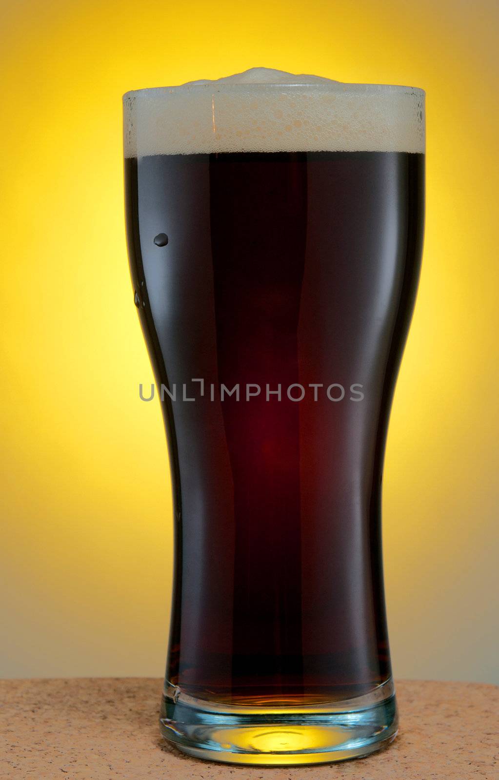 Glass of dark beer over yellow background