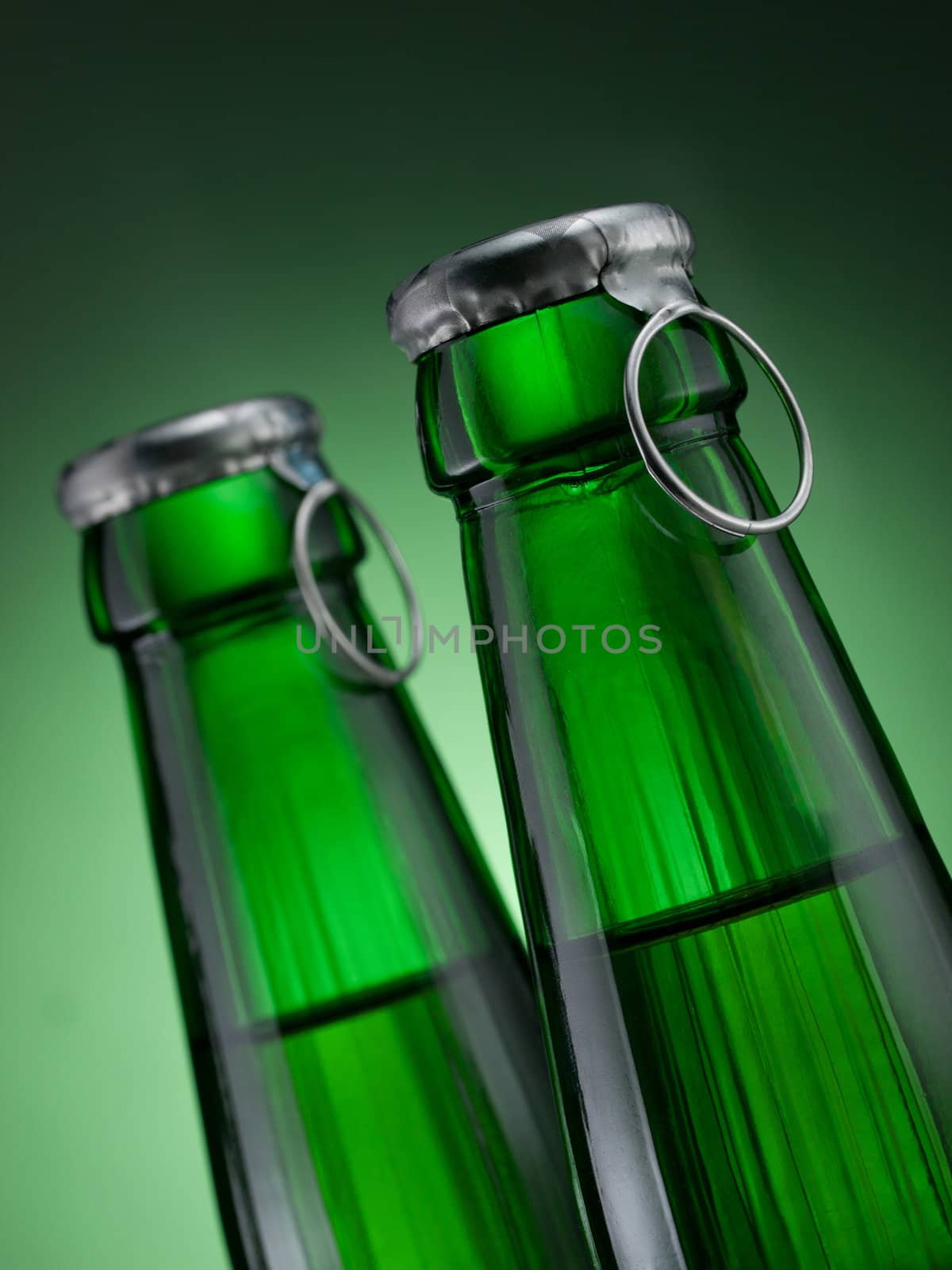 Two green bottles of beer on green background