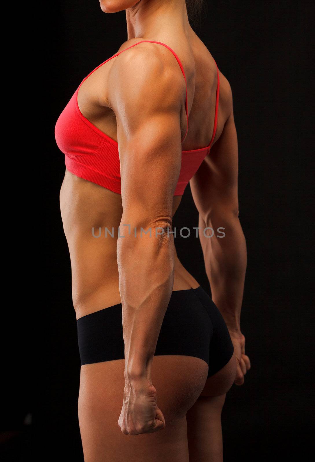 Female fitness bodybuilder posing against black background by Nobilior