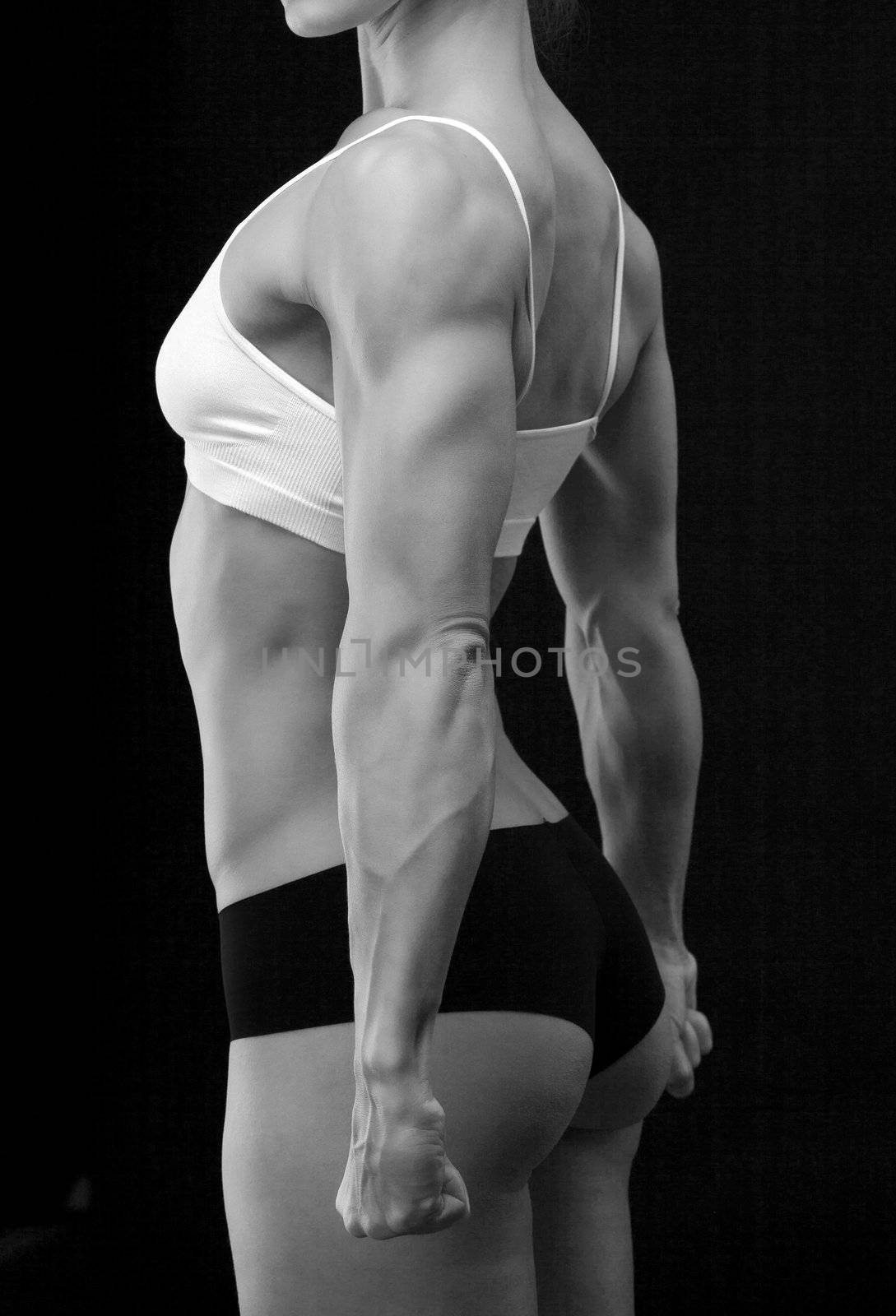 Female fitness bodybuilder posing against black background by Nobilior