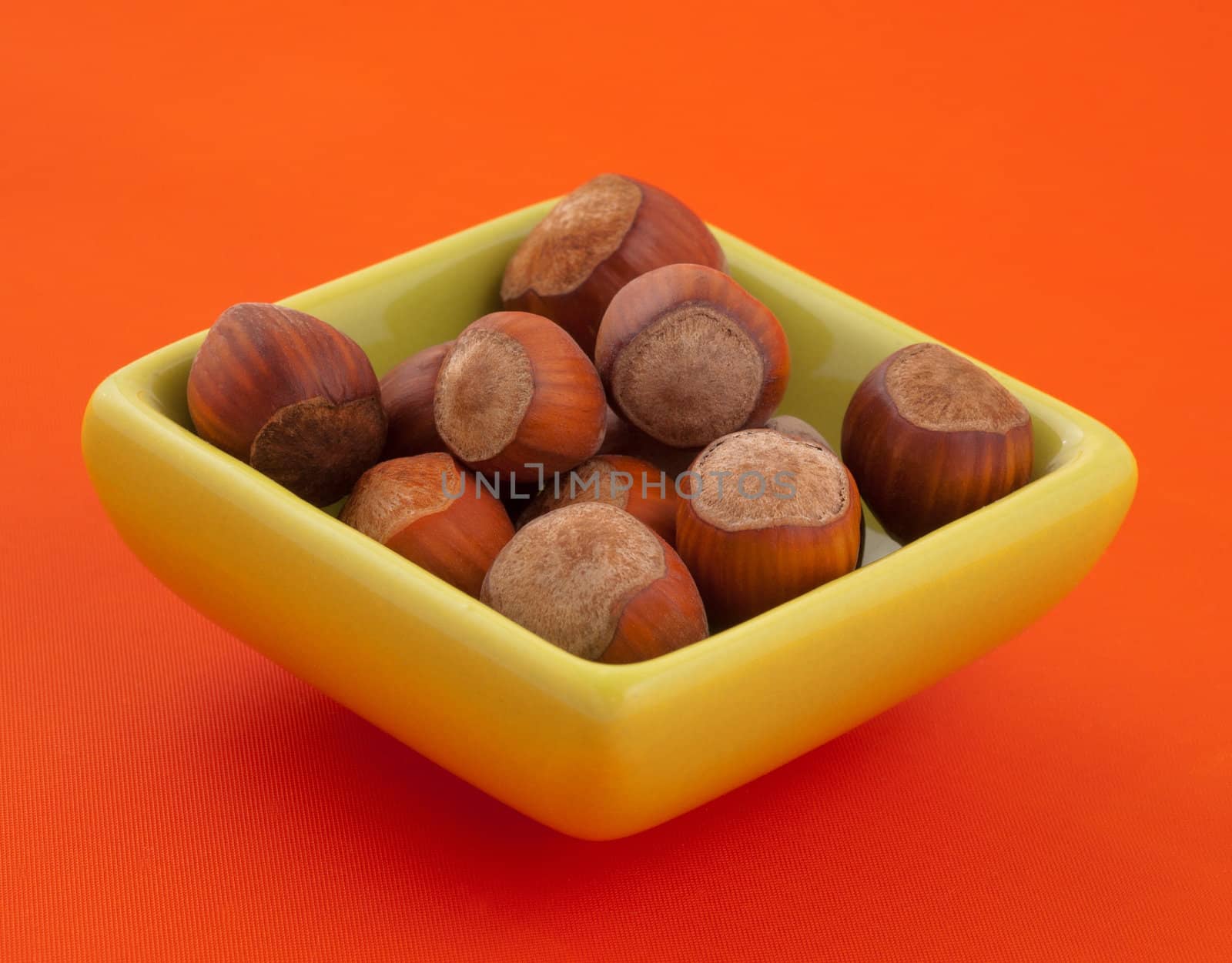 Group of hazelnuts in a bowl, with orange background and copy space.