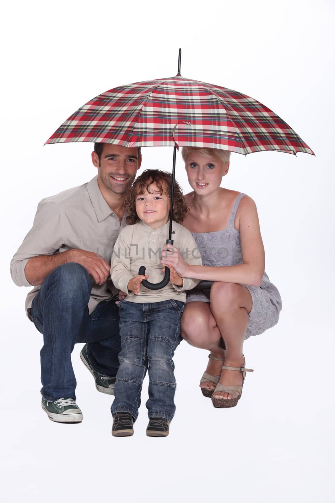 Young family crouching under an umbrella