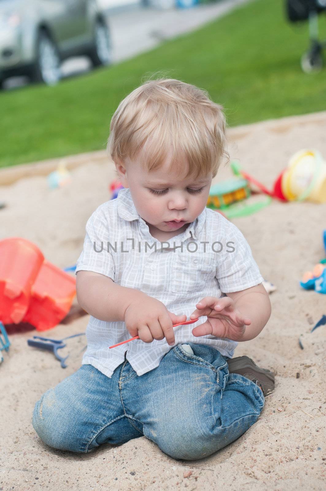 Small boy playing outside in playground with sand and toys