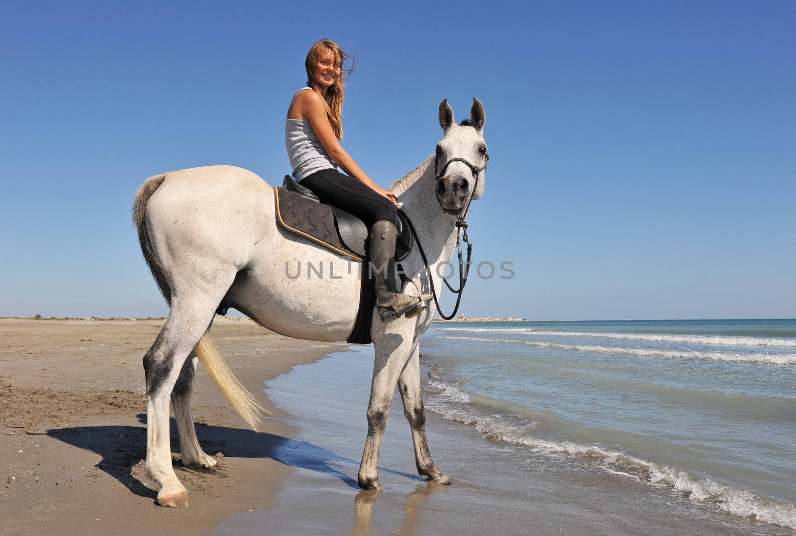 smiling riding teenager and her white horse on the beach