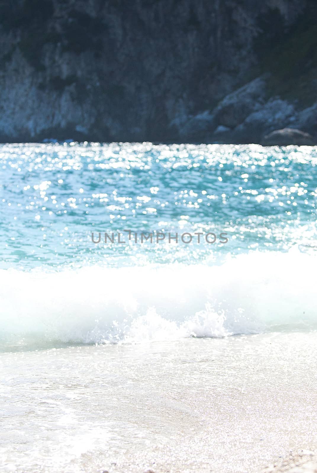 crashing waves of turqoise sea on beach, capri, italy with rugged cliffs in background