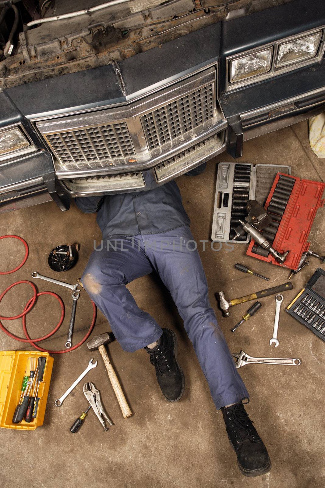 A mechanic doing repairs under the front of an old car from the early 80's.
