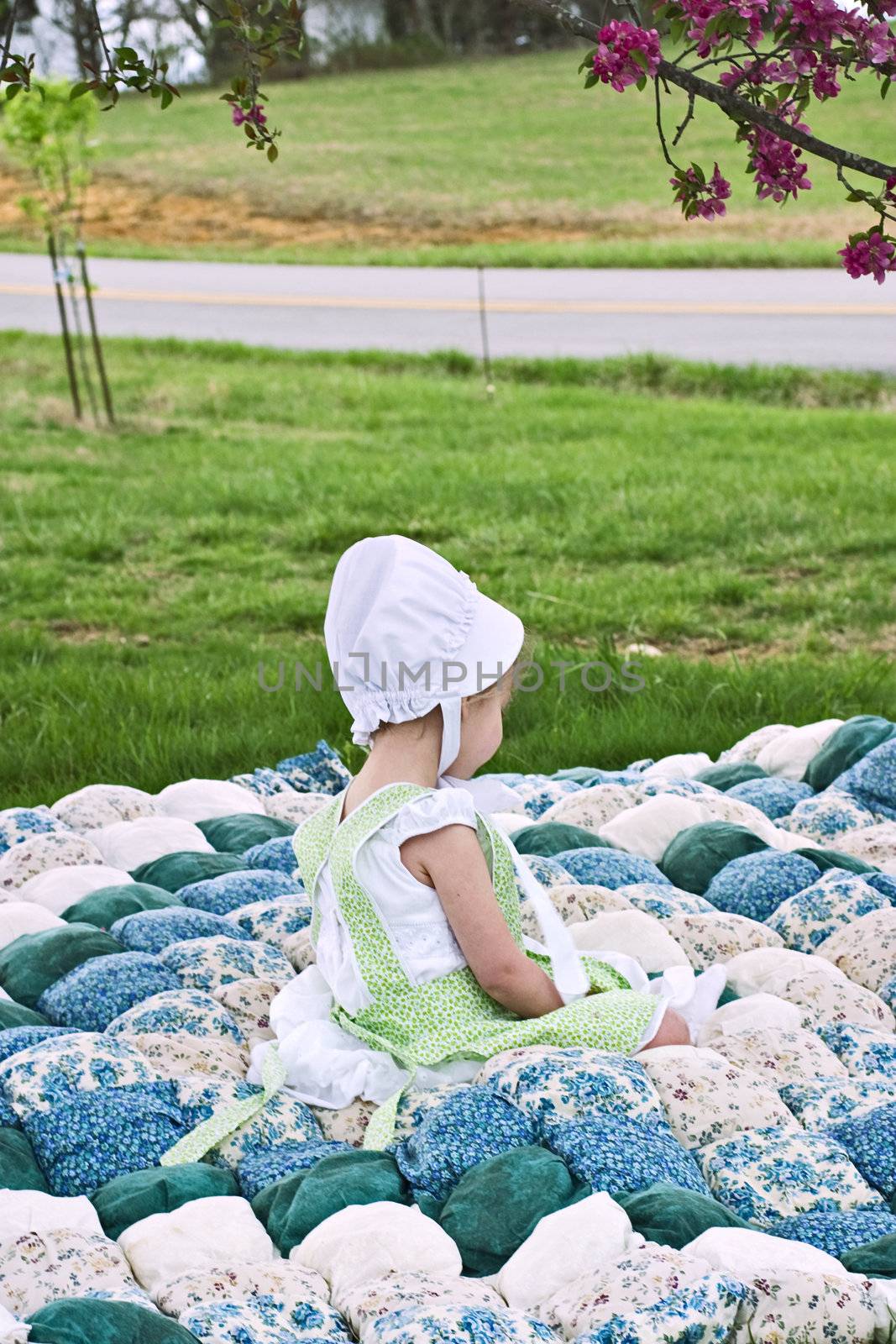 Amish child sitting on an old biscuit quilt.