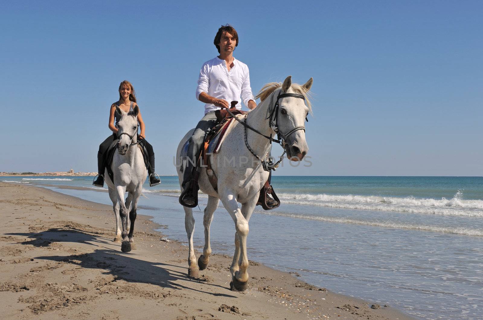 father and daughter are riding with their white horses on the beach