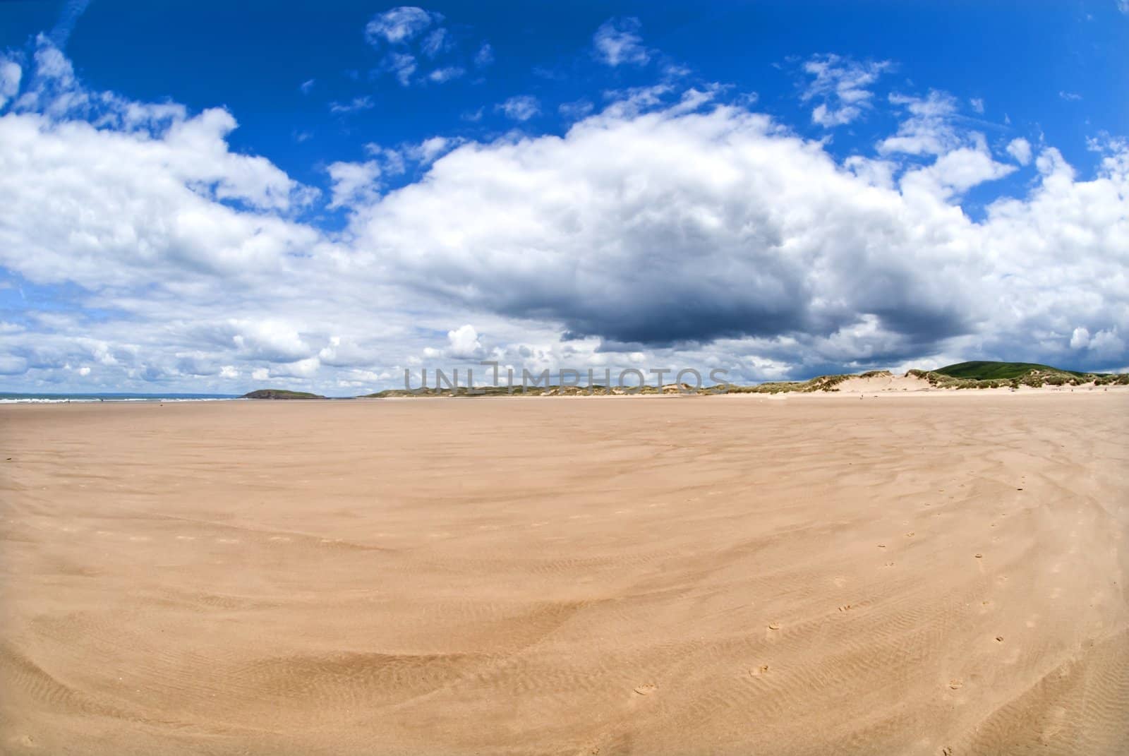 wide empty beach gower wales with blue skies and white clouds