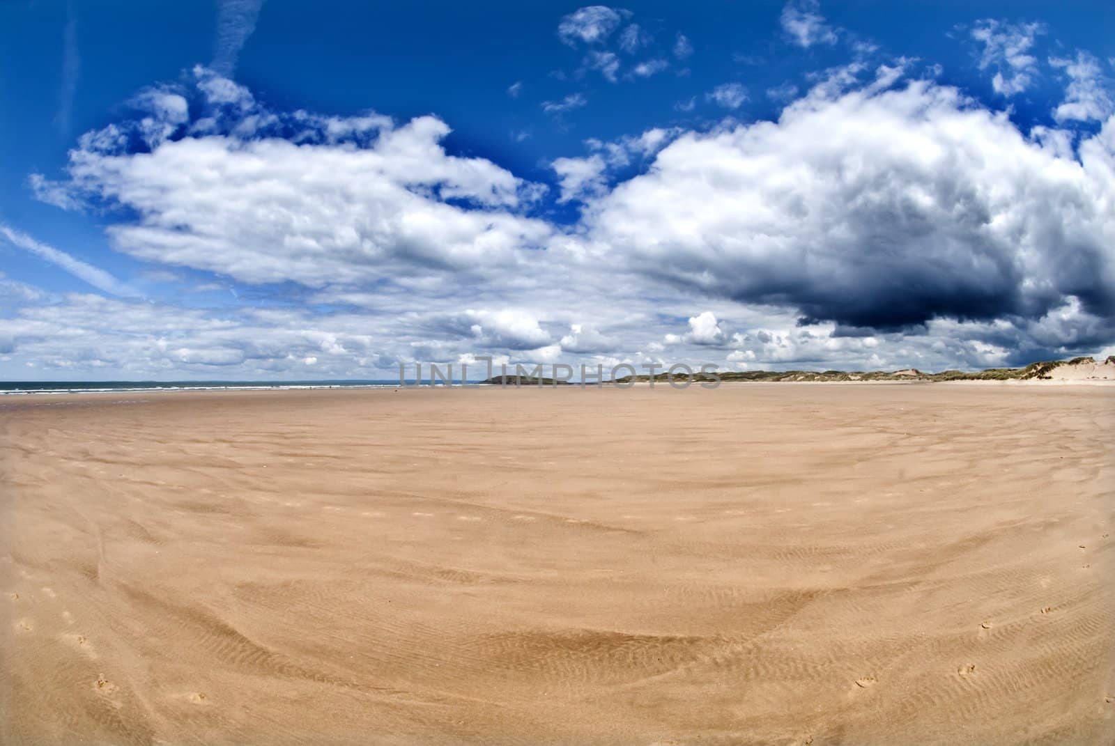 wide empty beach gower wales with blue skies and white clouds