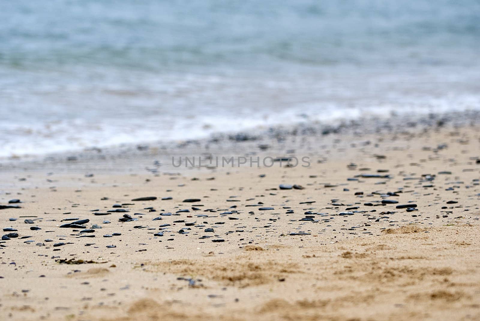 black stones on sandy beach with sea behind, newquay, cornwall