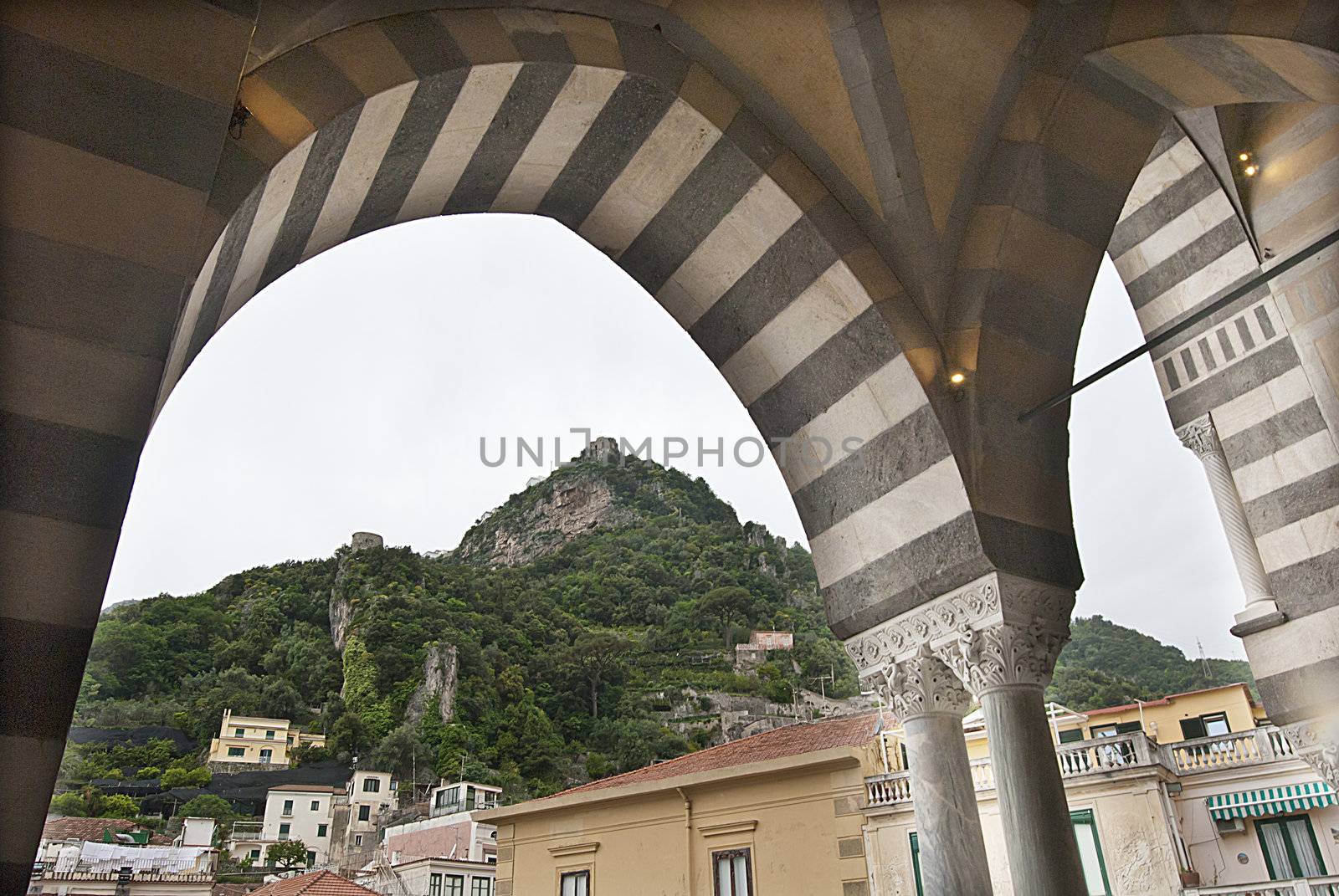 looking through decorative arches to house on top of hill amalfi by itsrich