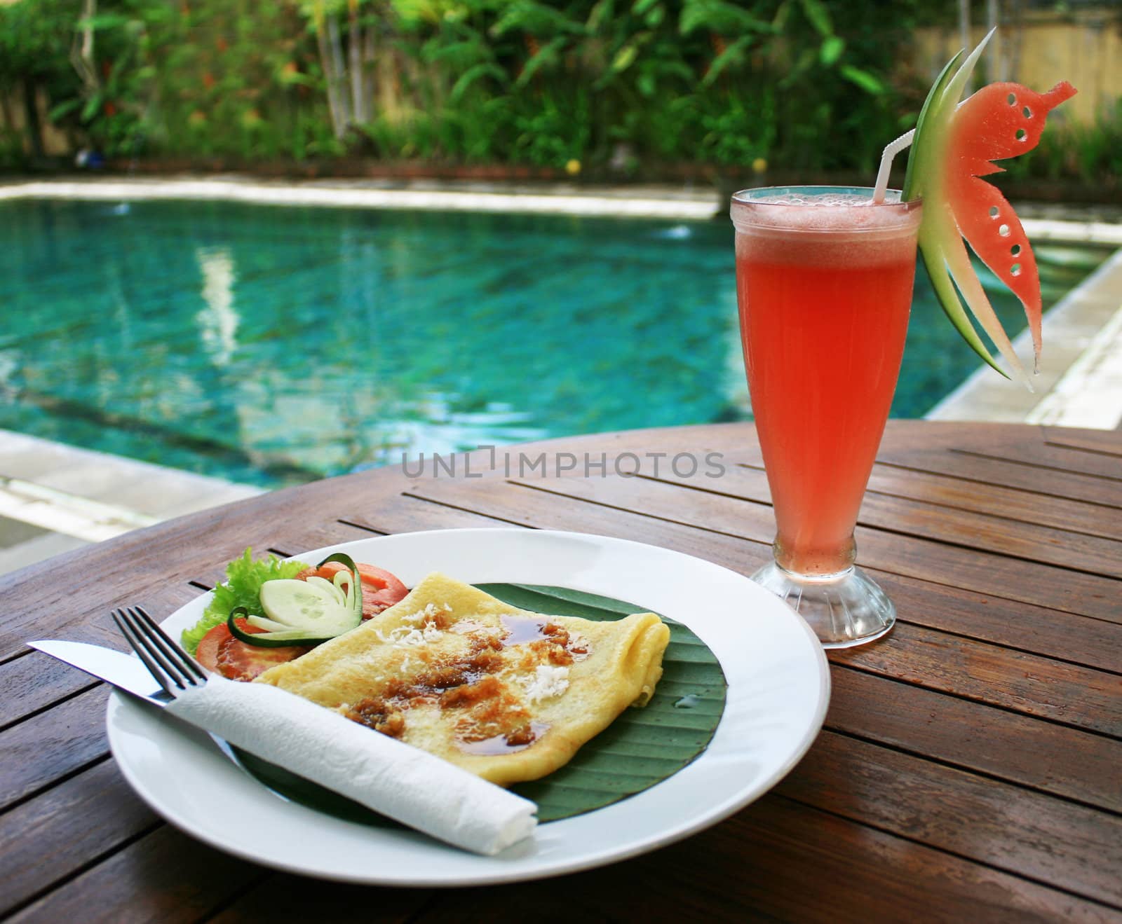 Breakfast set with banana pancake and watermelon juice beside pool.