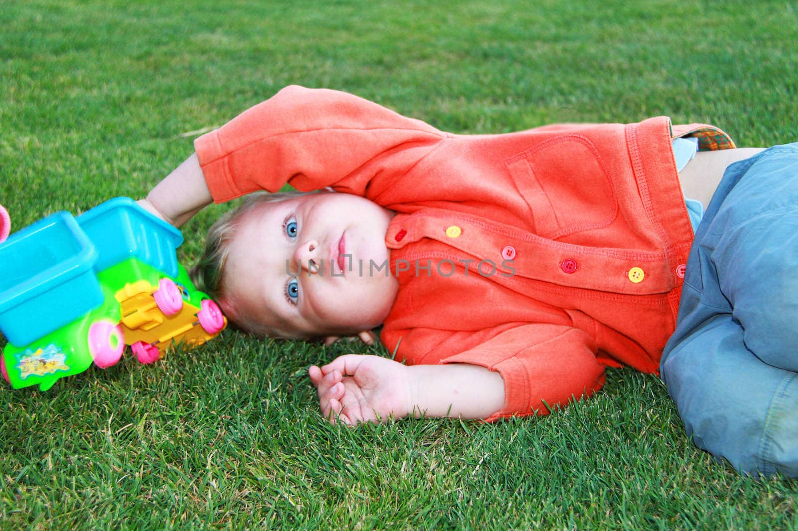 Baby lying on the grass with a toy