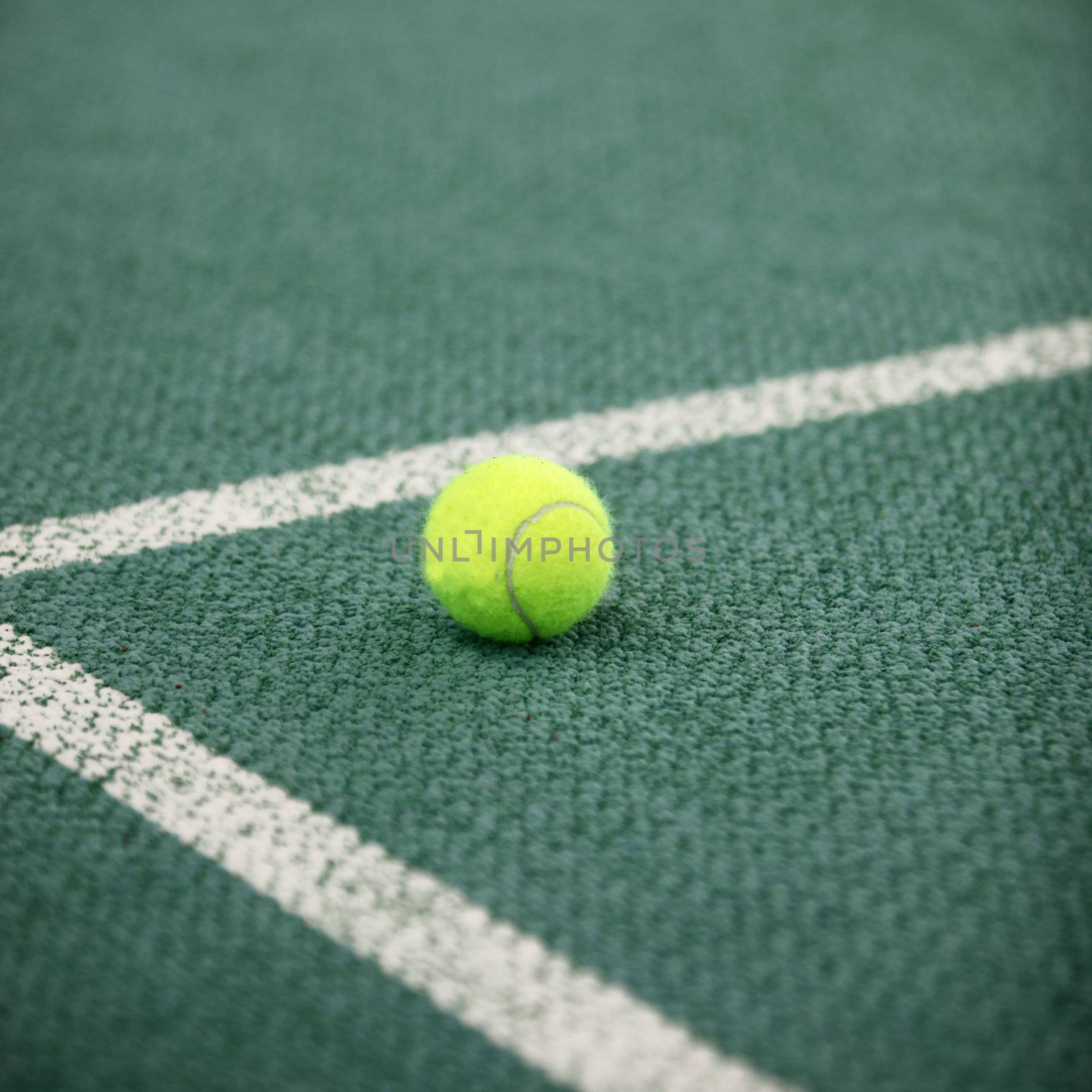 Luminous green high visibility tennis ball on a green tennis court lying in the angle of the lines forming the corner