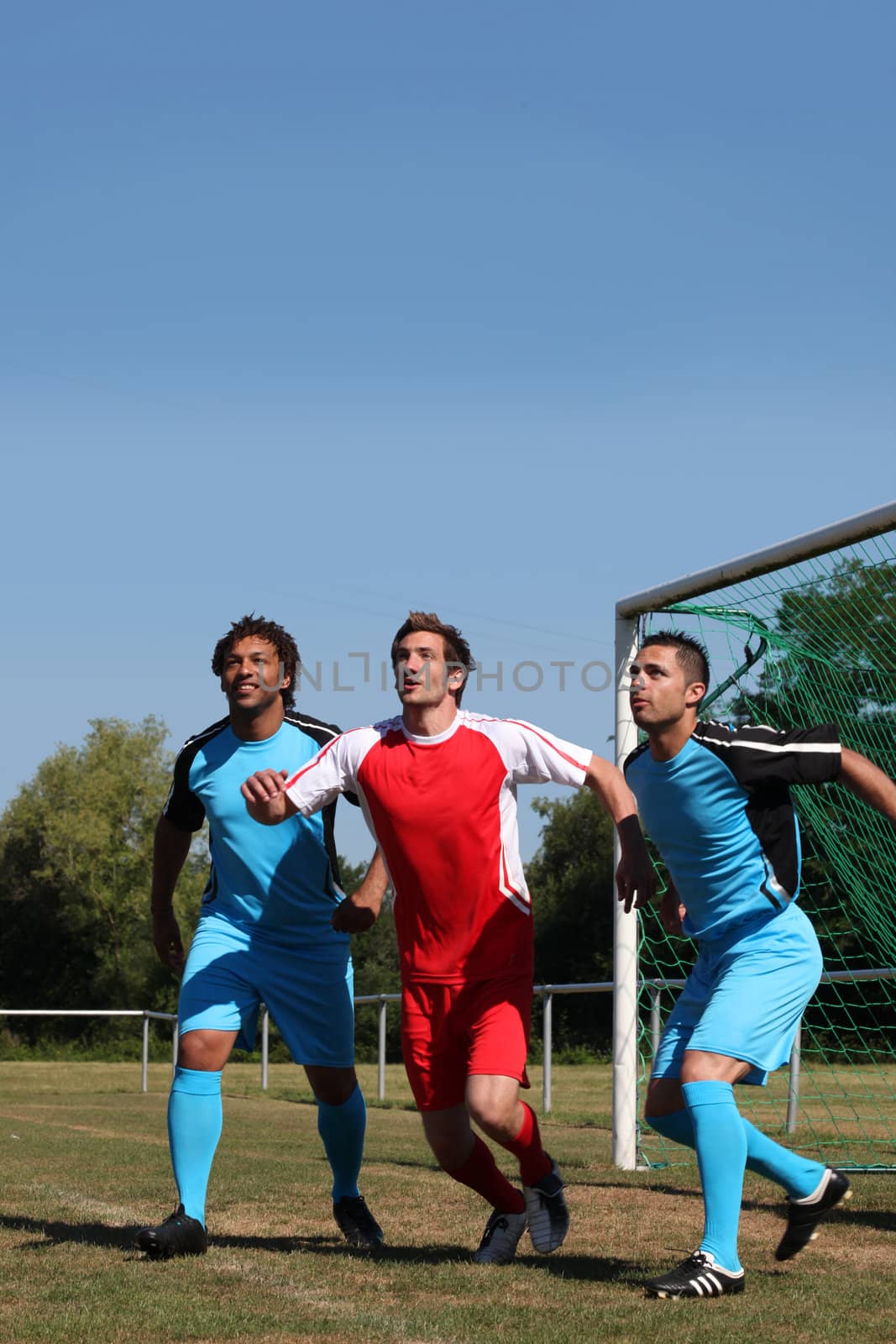 Three footballers waiting for the ball in front of goal by phovoir