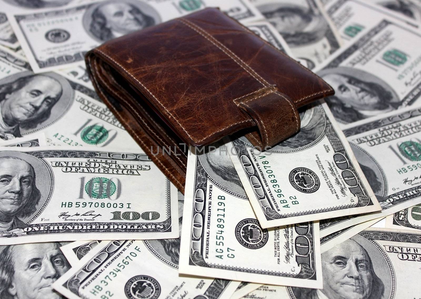 leather purse lying among the one hundred dollar notes on white background