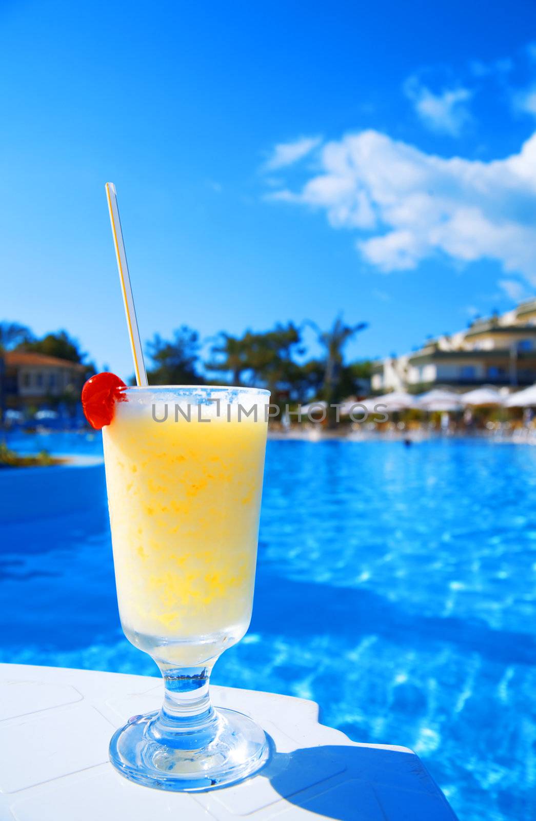 cocktail in glass with a cherry on a background blue water of pool