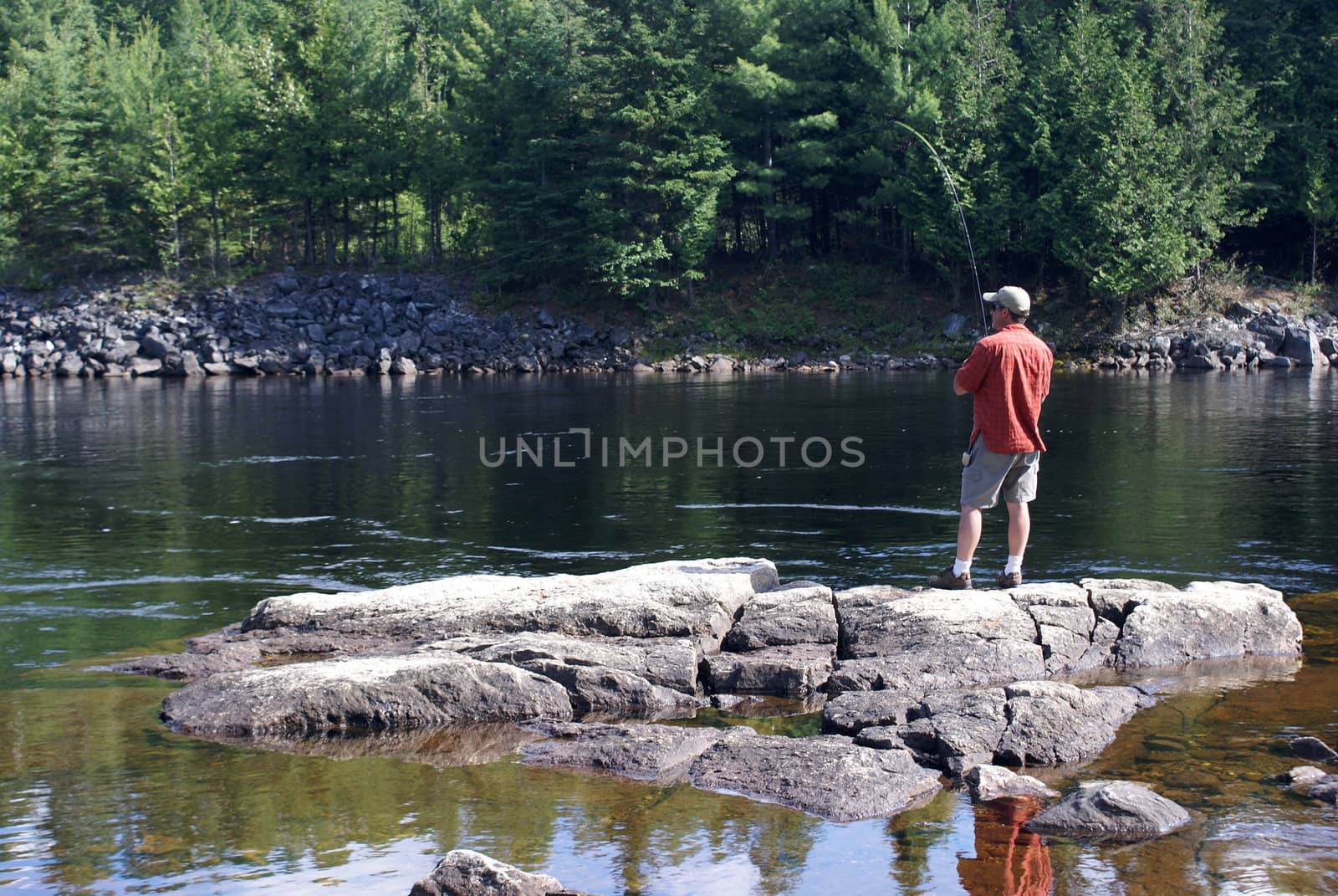A fisherman stands on some rocks as he reels in his lure.