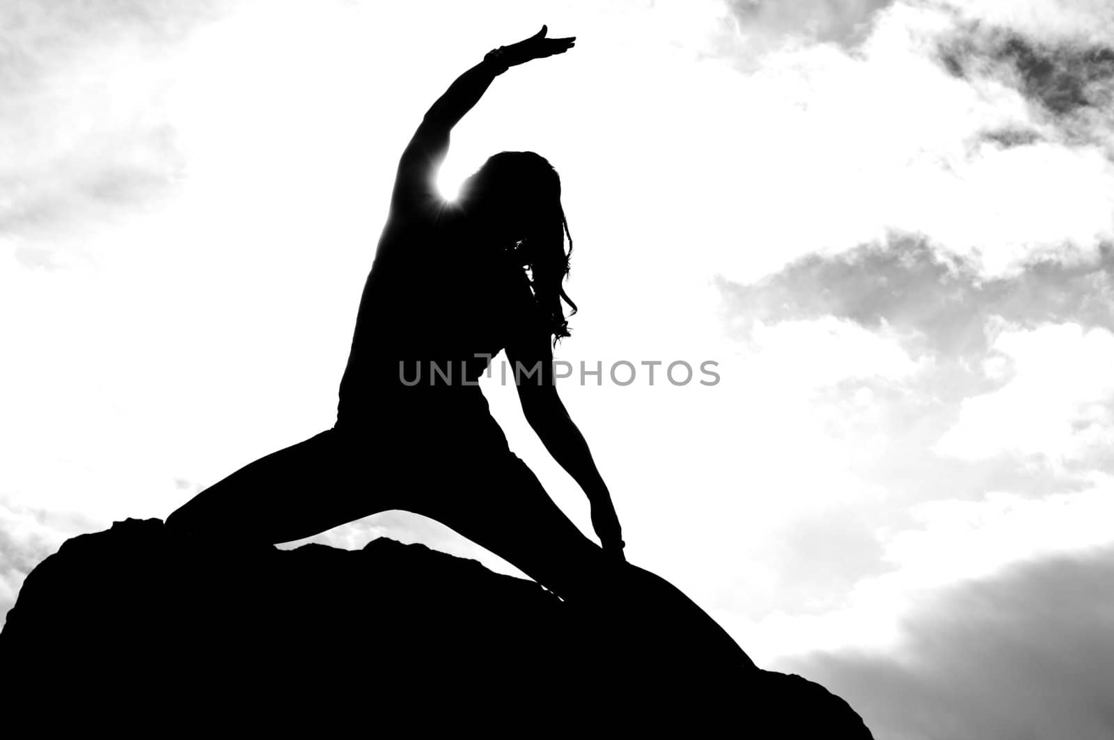 Black and white silhouette of young attractive girl doing yoga on top of a rock with the sky and cloudy in the background
