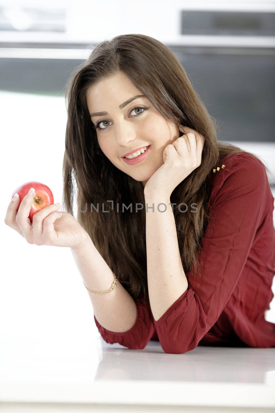 Beautiful young woman eating an apple in her white kitchen