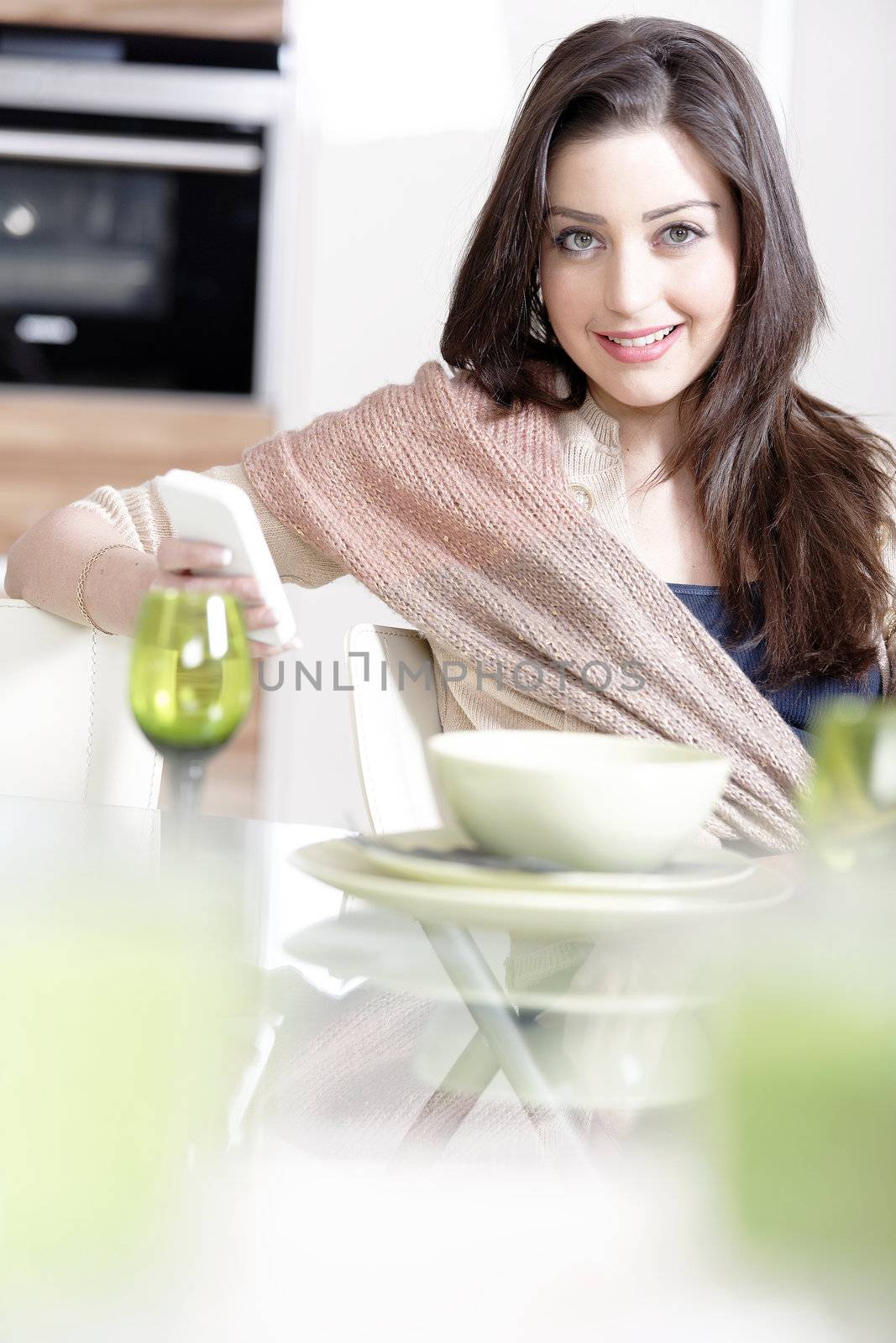 Beautiful young woman chatting on her mobile phone in her kitchen