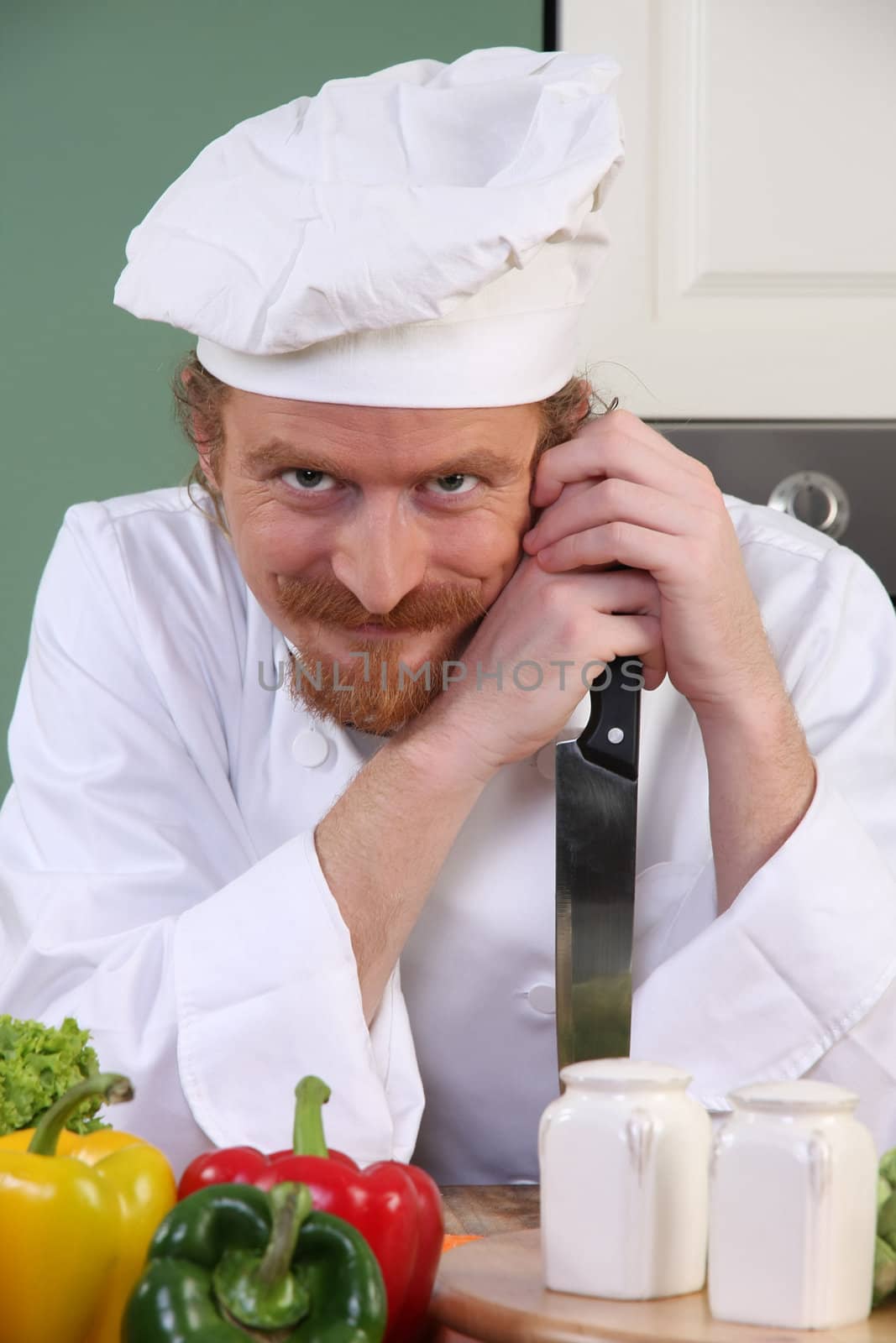 Funny young chef with a knife in kitchen 