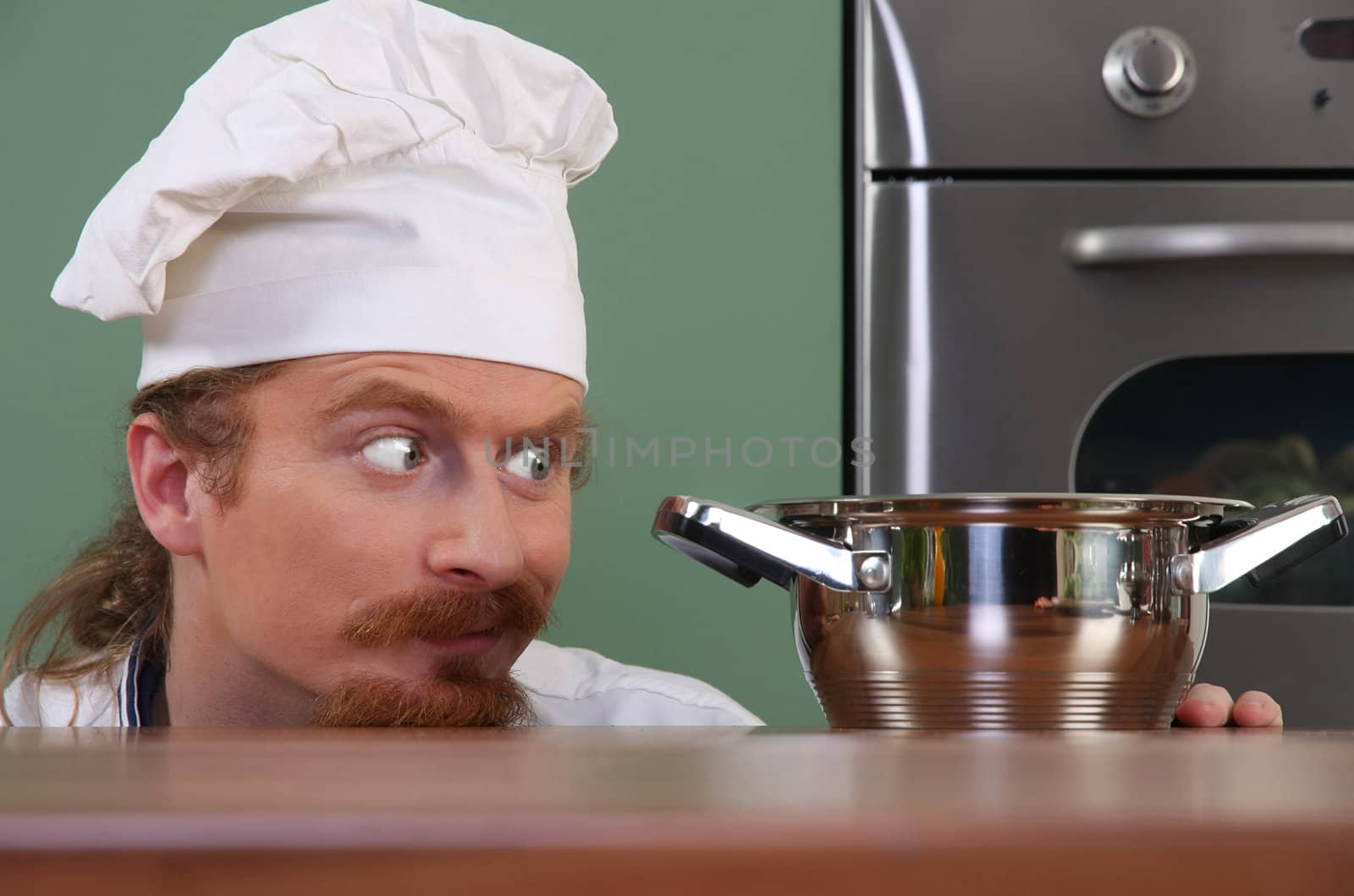 Funny young chef strange looking at pot