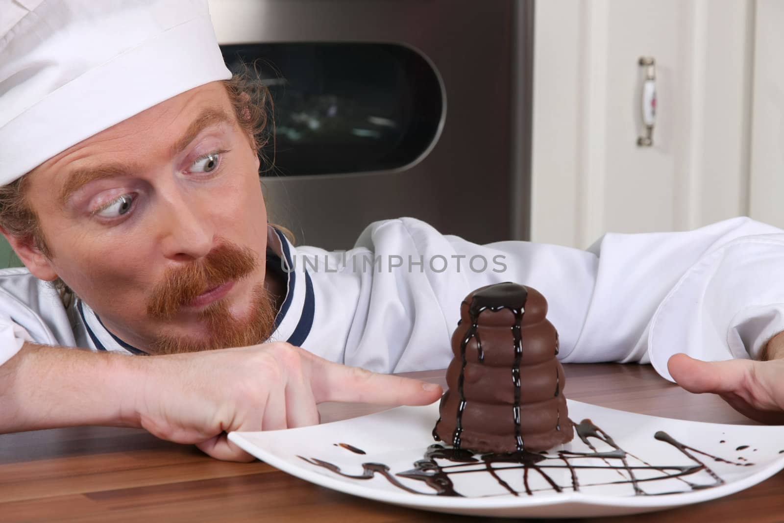 Funny young chef strange looking at piece of cake with chocolate sauce 