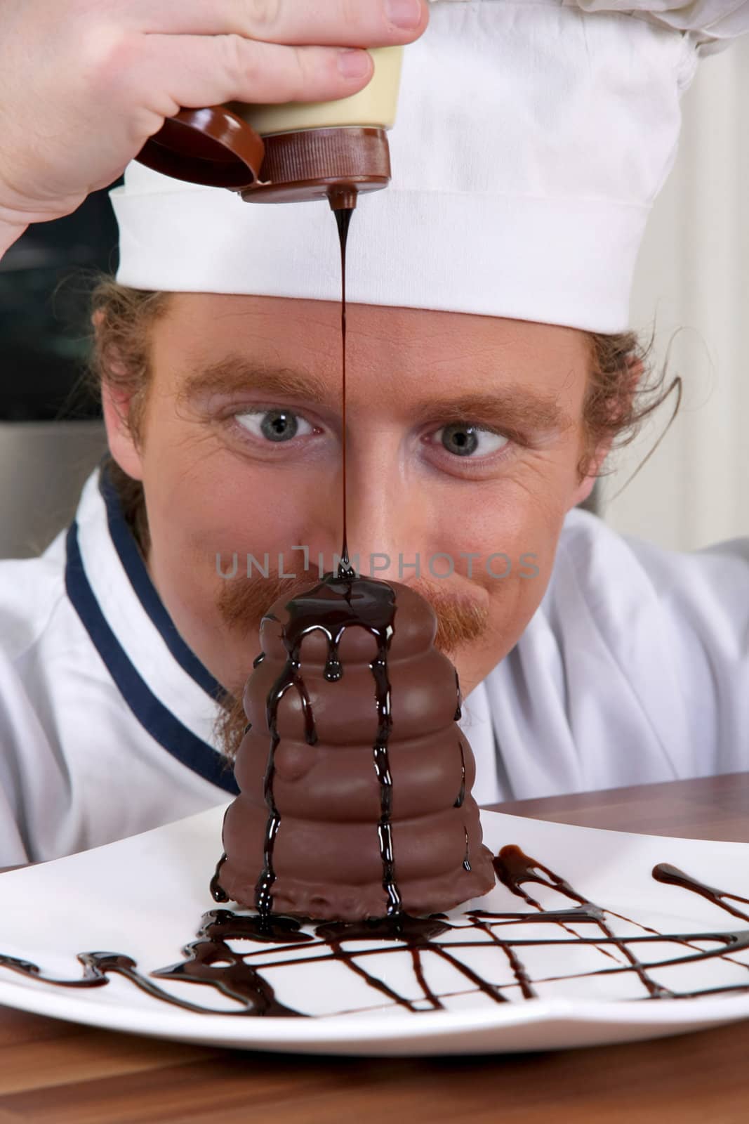 Funny young chef added chocolate sauce at piece of cake