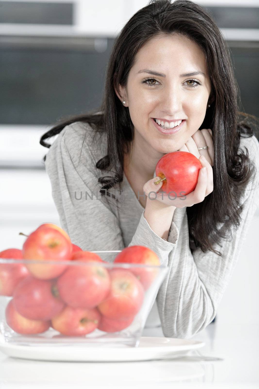 Beautiful young woman eating an apple in her white kitchen relaxing