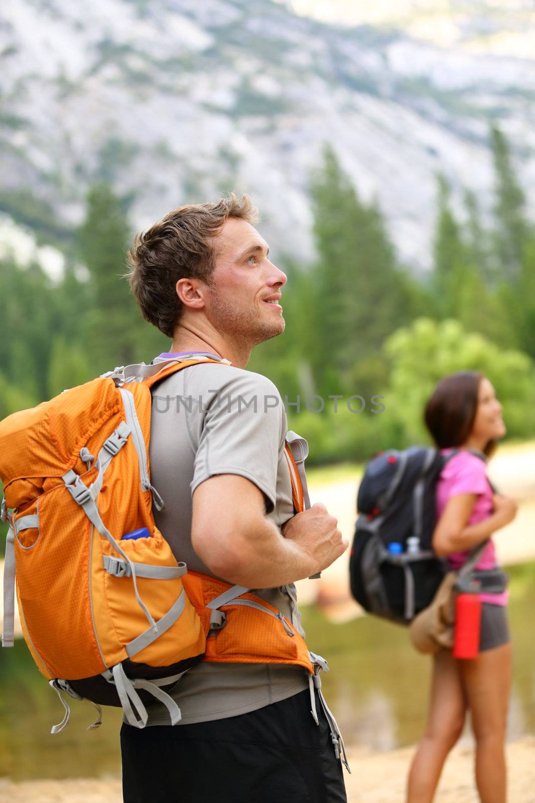 Hiking people - man hiker looking at landscape nature with mountains and woman in background. Happy multiracial young couple trekking outdoors in Yosemite National Park., California, United States.