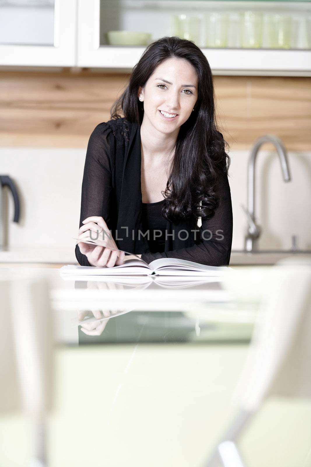 Beautiful young woman reading from a recipe book in her kitchen