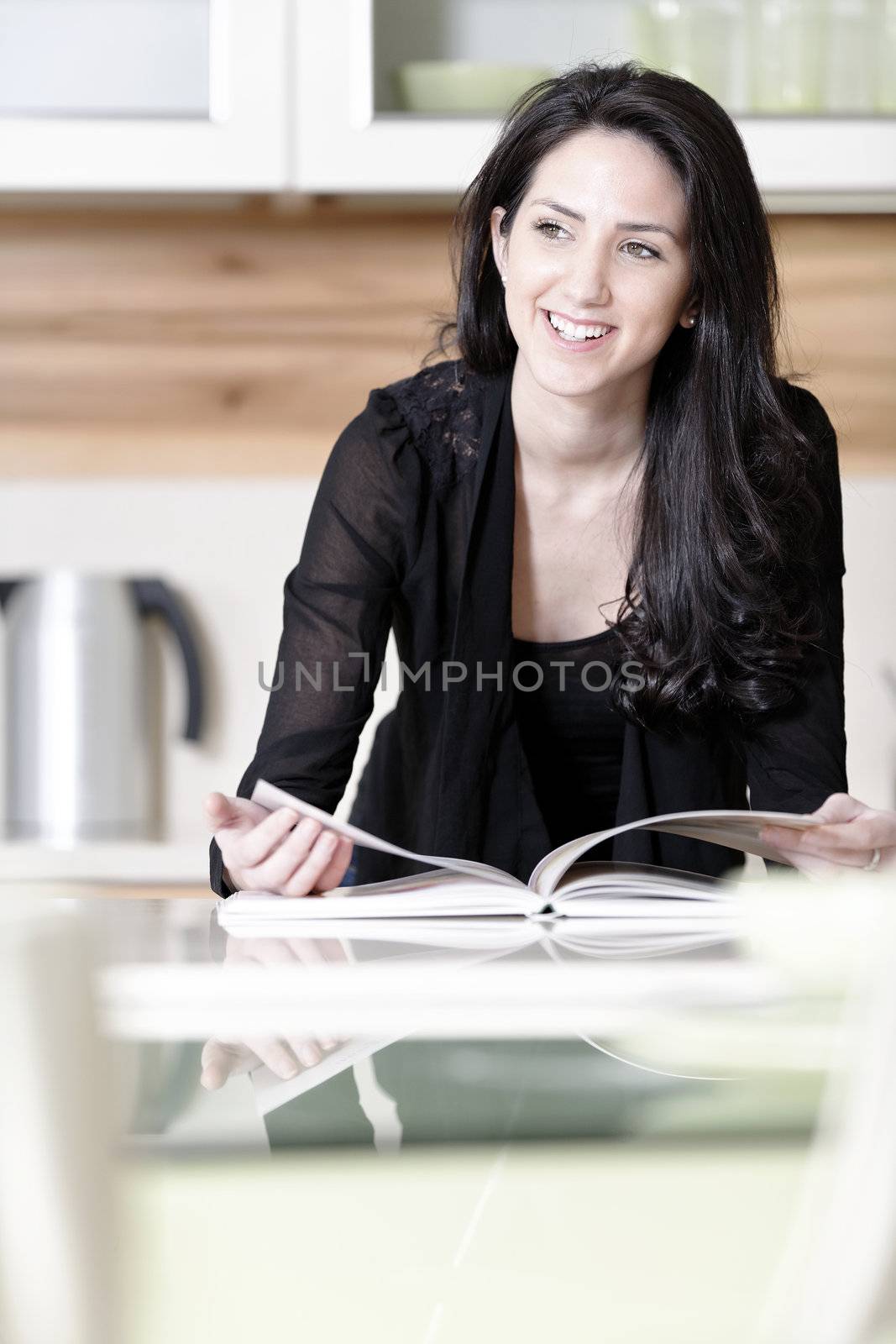 Beautiful young woman reading from a recipe book in her kitchen