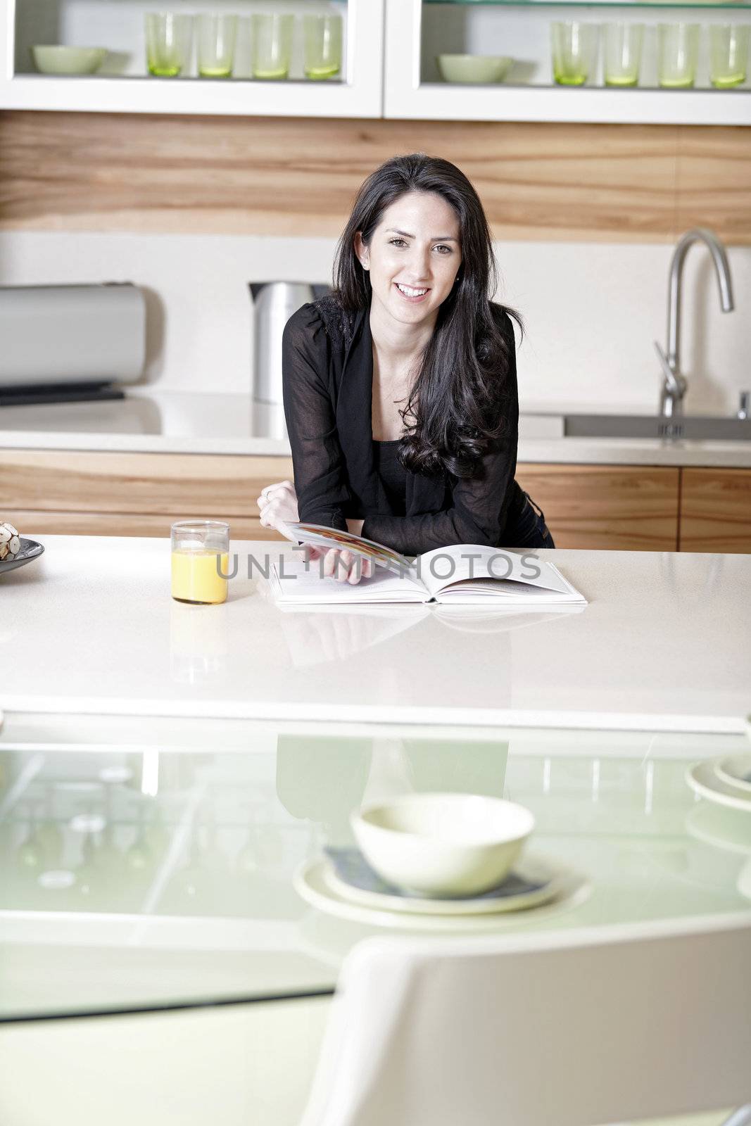 Beautiful young woman reading from a recipe book in her kitchen