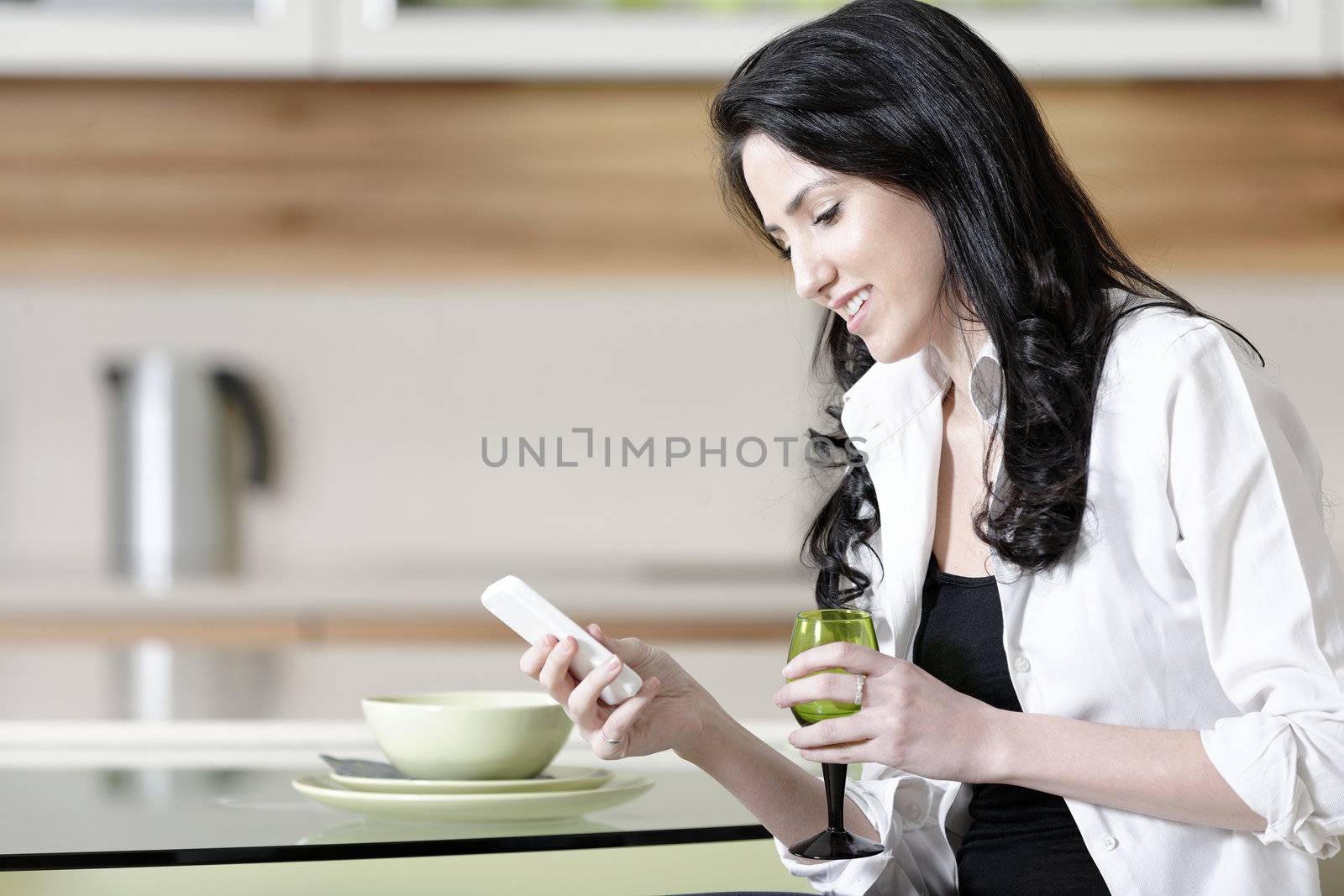 Beautiful young woman chatting on her mobile phone in her kitchen