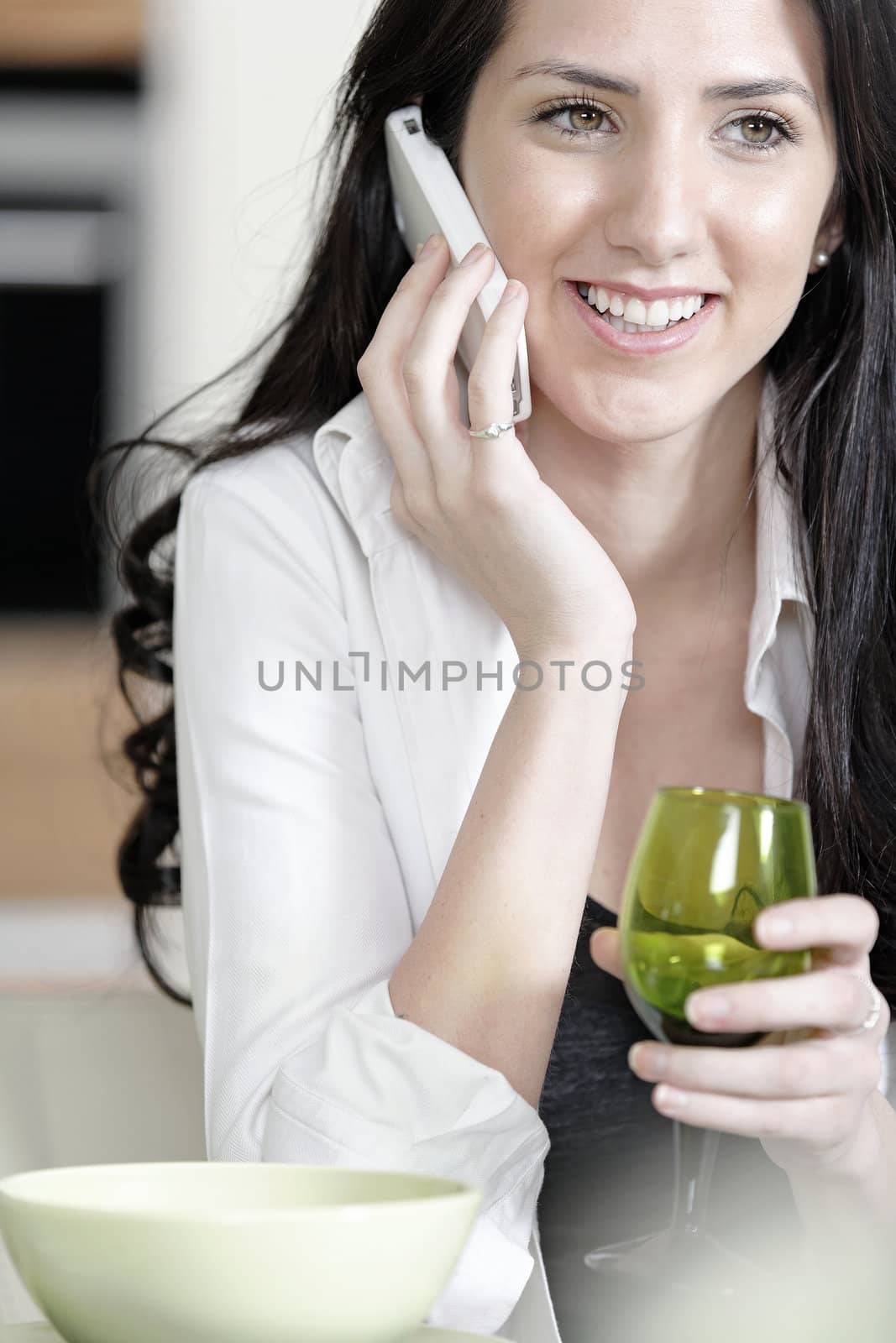 Beautiful young woman chatting on her mobile phone in her kitchen