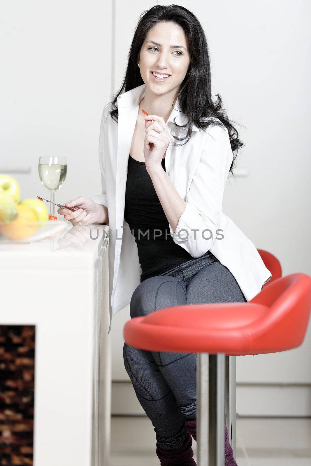 Beautiful young woman enjoying a glass of wine in her kitchen, while preparing food.