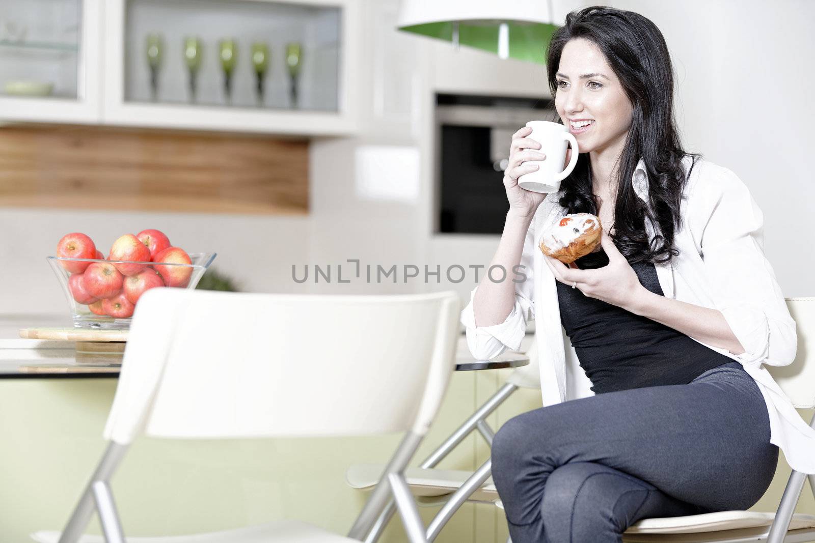 Beautiful young woman taking a break in her kitchen with a coffee and cake.