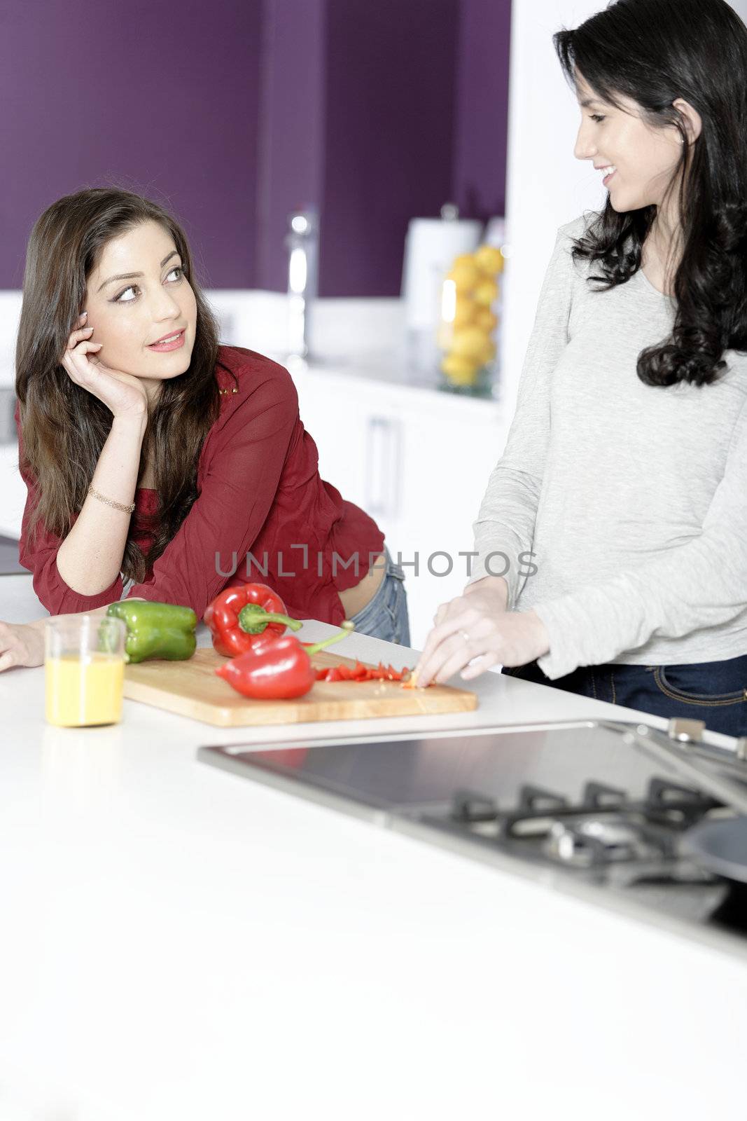 Two attractive young women preparing food in a white kitchen while talking.